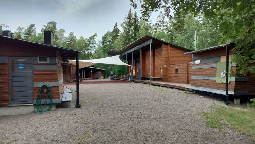 Edustalla hiekka-alue, taustalla puiset rakennukset, joiden välissä purjekatos.