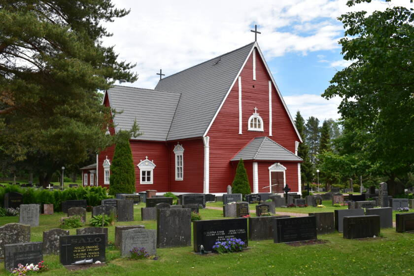 Etualalla hautakiviä, taustalla punainen puukirkko.