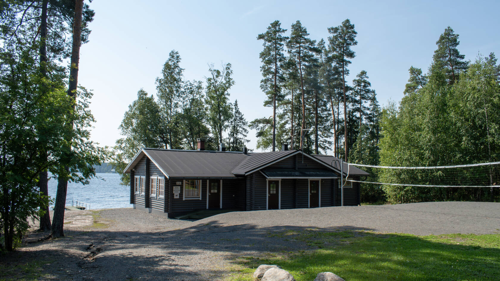 Etualalla polku ja nurmikkoa, takana järvenranta ja mökki.