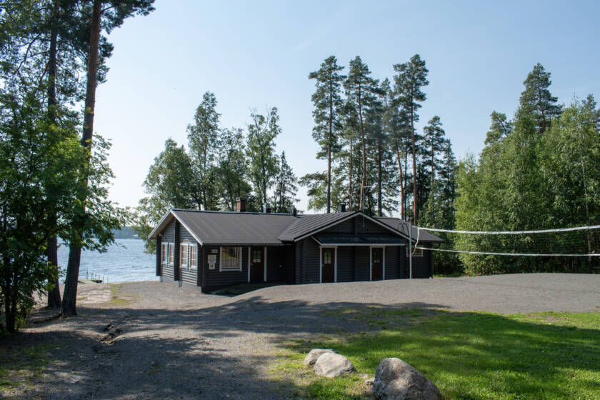 Etualalla polku ja nurmikkoa, takana järvenranta ja mökki.