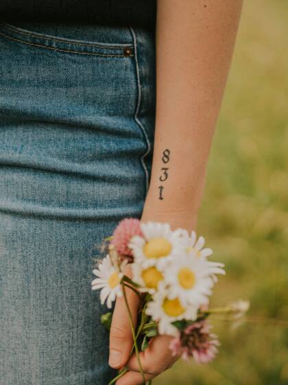 Etualalla luonnonkukkakippua pitelevä käsi, ranteeseen tatuoitu numero 831.
