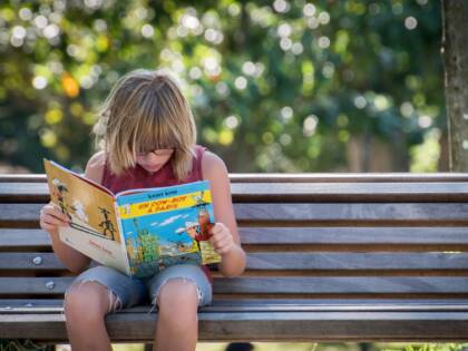 Lapsi istuu puistonpenkillä lukemassa.