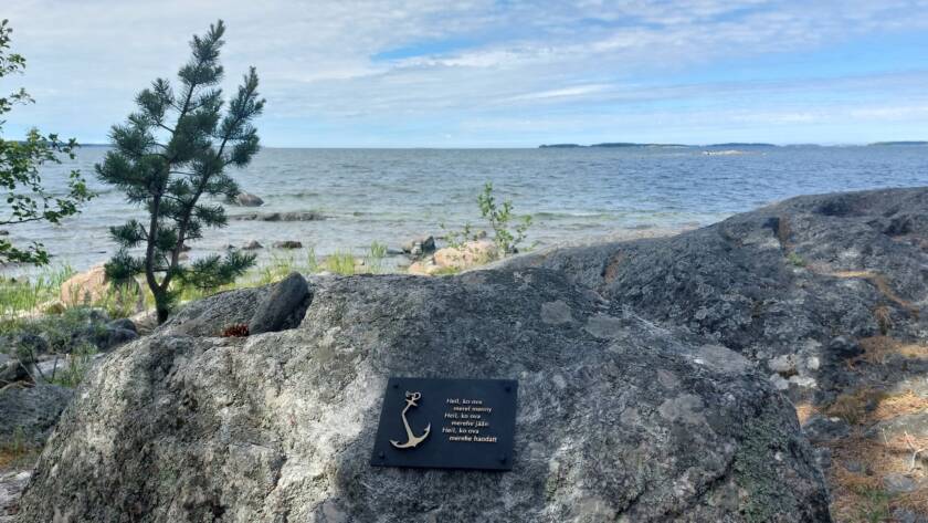 Kallio, johon on kiinnitetty muistolaatta. Taustalla merta.