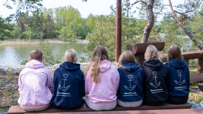 Nuoria istumassa rivissä. Päällä hupparit, joiden selässä näkyy ankkurikuvio.