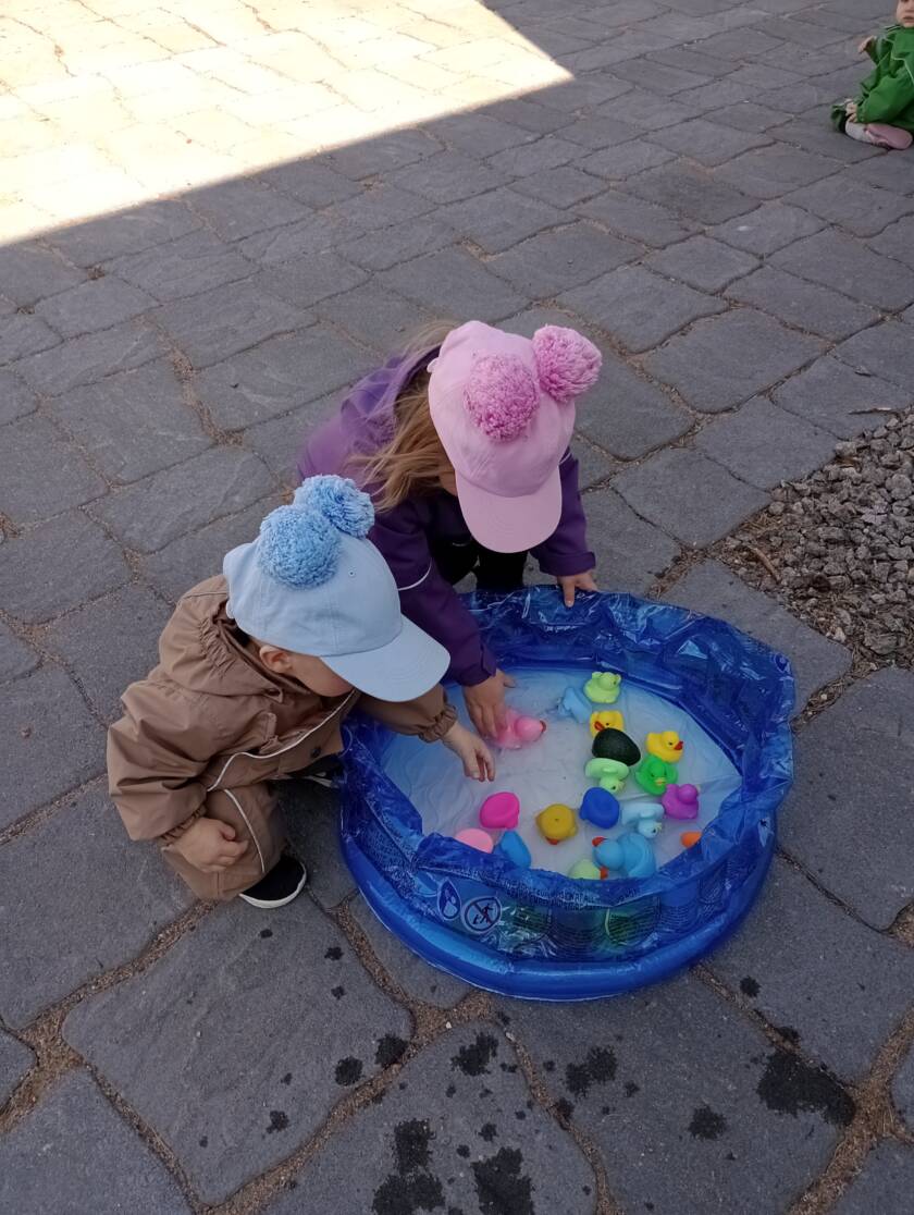 Kaksi lasta kyykyssä pienen uima-altaan vieressä, altaassa värikkäitä palloja.