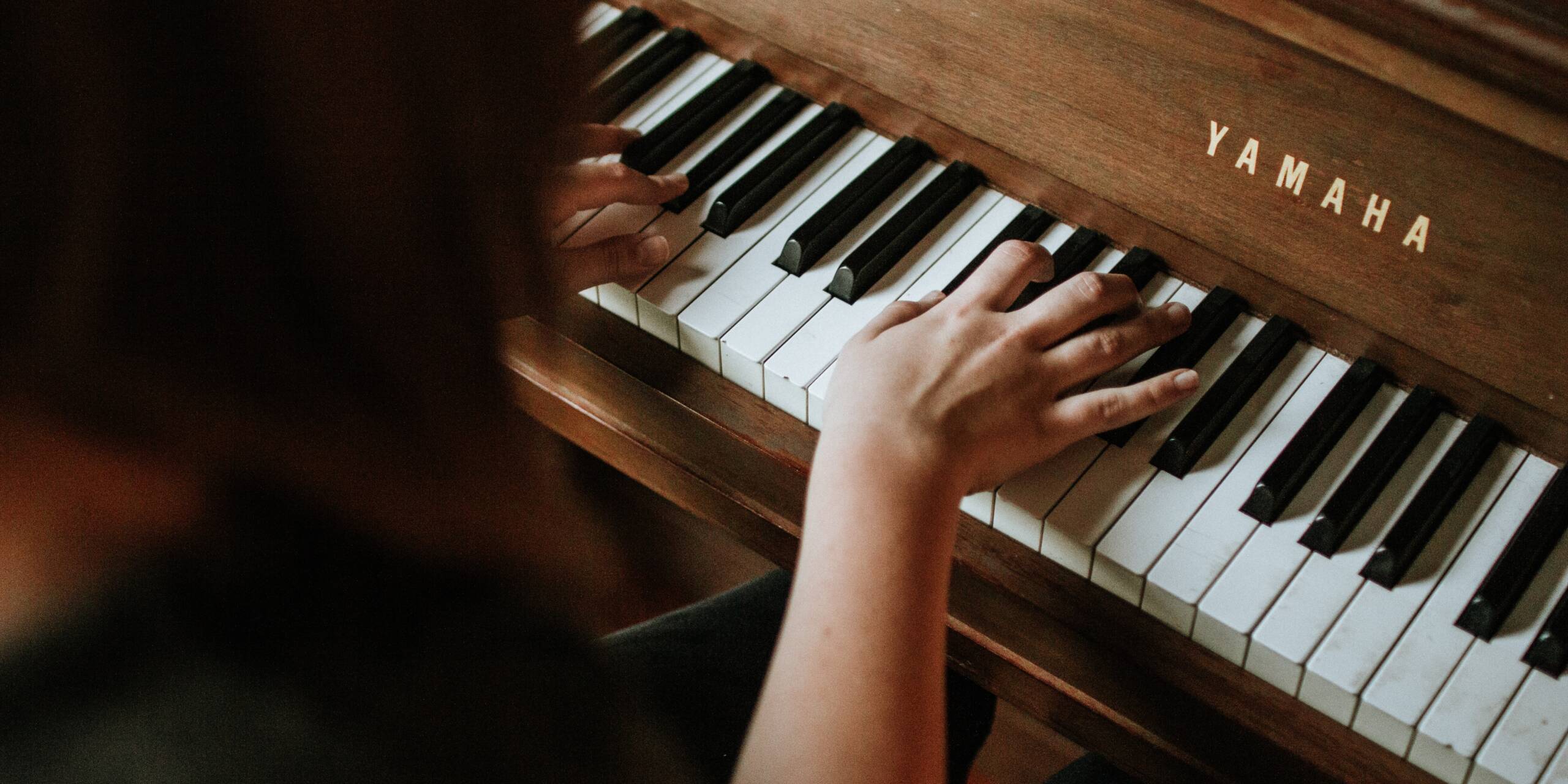 Nainen soittaa pianoa, kädet koskettimilla.