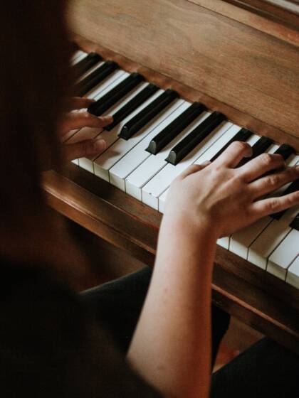 Nainen soittaa pianoa, kädet koskettimilla.