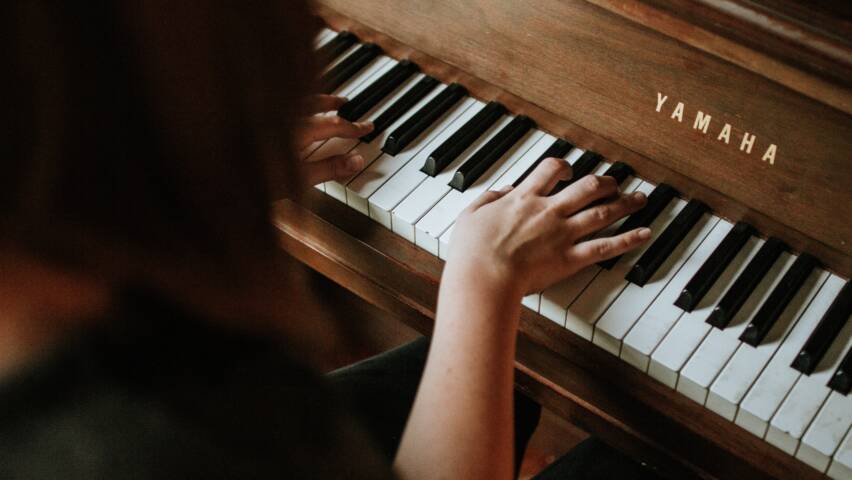 Nainen soittaa pianoa, kädet koskettimilla.