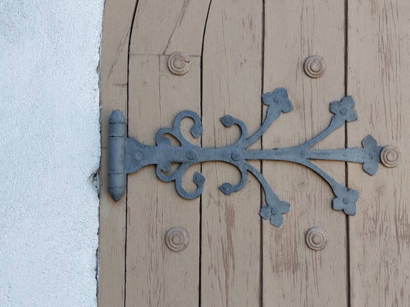 Koristeellinen taottu ovikoriste, joka lähtee saranasta.