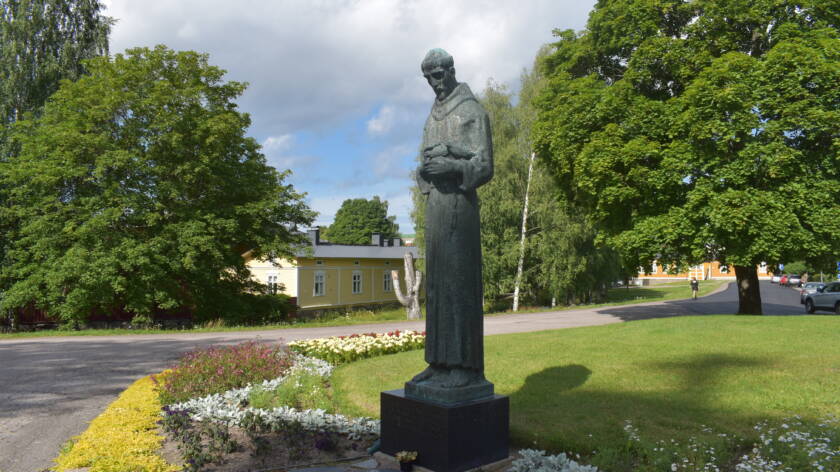 Pyhän Franciscuksen patsas, taustalla taloja ja puita.