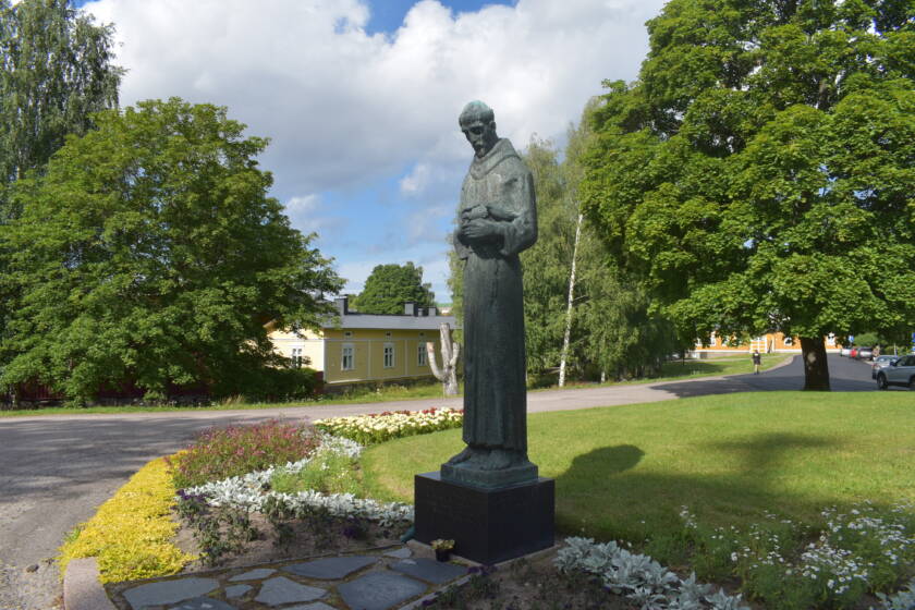 Pyhän Franciscuksen patsas, taustalla taloja ja puita.