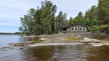 Järven rantaa ja rannalla kallioita, puita ja sauna.