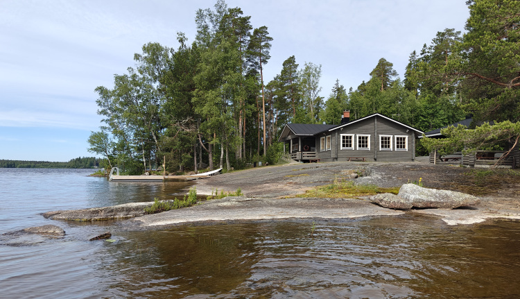 Järven rantaa ja rannalla kallioita, puita ja sauna.