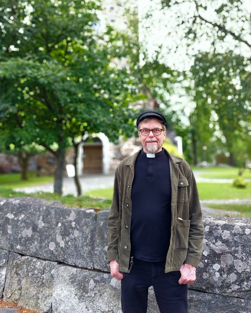 Mies seisoo kivimuurin edessä hymyillen.