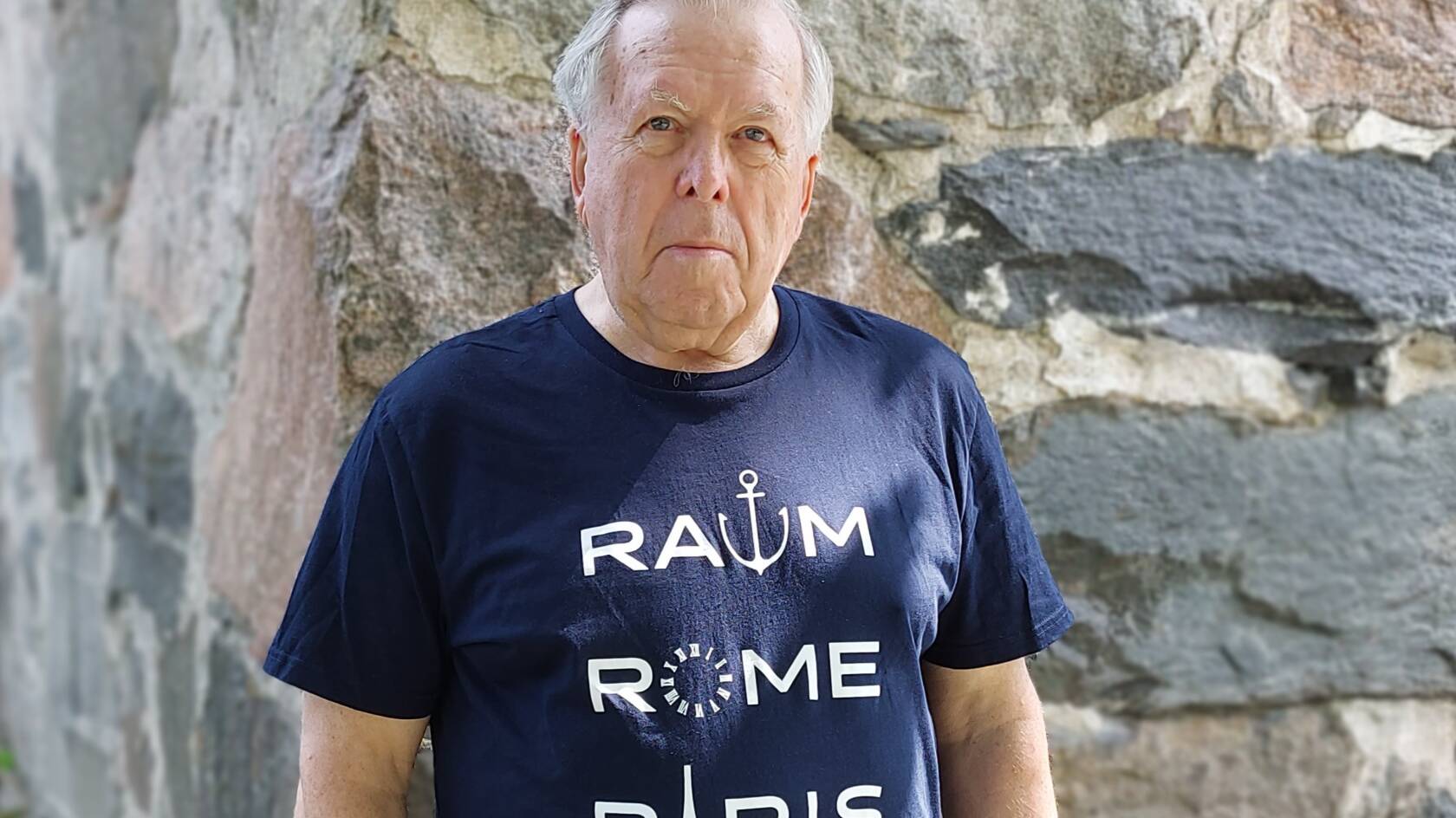 Mies seisoo vasten kiviseinää.