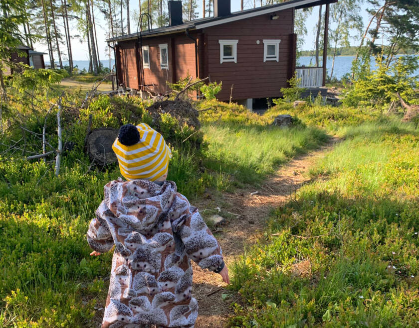 Lapsi kulkee polulla, taustalla meri ja mökki.