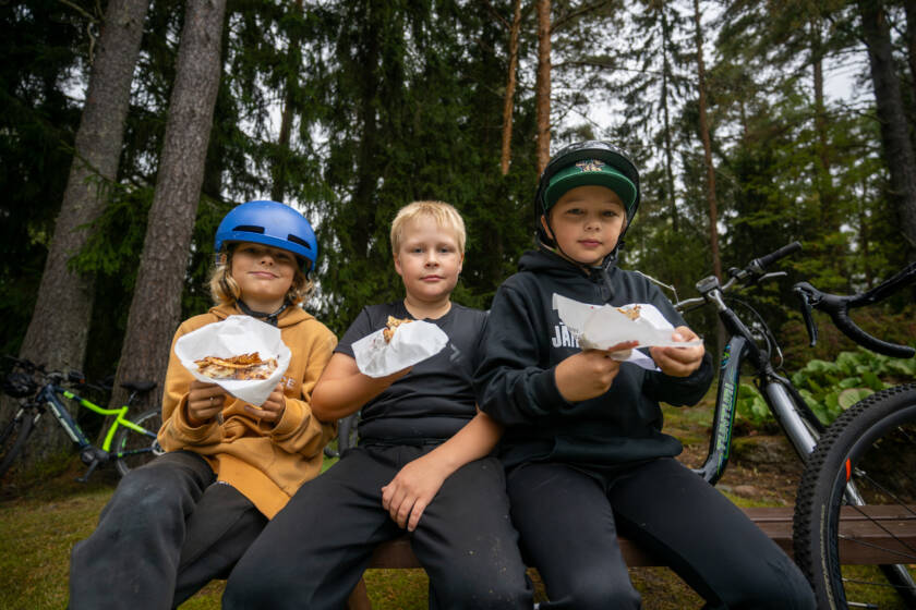 Kolme poikaa rivissä syömässä lettuja.